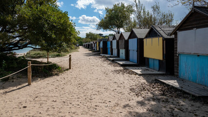 Wooden, shuttered beach huts facing out across a tree lined beach to the sea