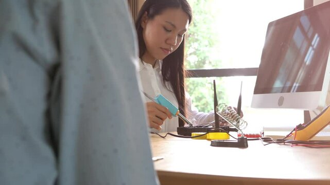A man and a woman are working on a project together. The woman is holding a tool and the man is looking at a computer monitor. Scene is collaborative and focused