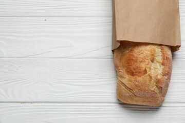 Paper bag with fresh baguette on white wooden table, top view. Space for text