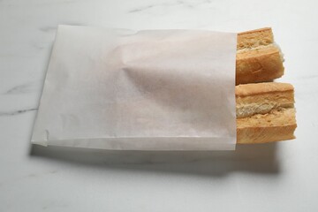 Paper bag with fresh baguette on white marble table, above view