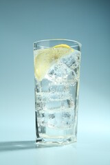 Soda water with lemon and ice cubes in glass on light blue background