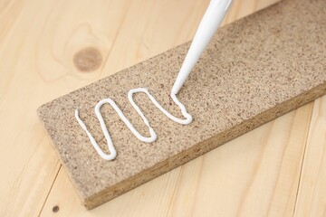 Glueing wooden plank with caulking gun at table, closeup