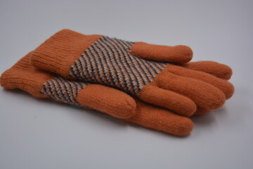 Warm, soft, winter items and household items. Beautiful orange, gray, insulated, knitted gloves are located on a white plastic background.