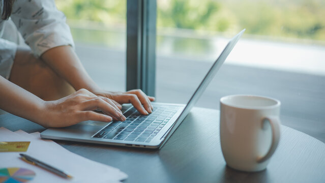 Businesswoman typing on laptop computer keyboard on wood desk at office, Technology, Business concept. Business woman analyze the graph of the company performance to create profits and growth.