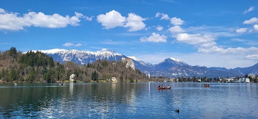 A breathtaking view of Lake Bled, Slovenia. The picturesque lake with its iconic Bled Castle perched atop a cliff, surrounded by snow-capped mountains and a clear blue sky.