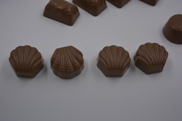 Food, food, very tasty milk candies are located on white plastic. Chocolates are made in the form of leaves, walnuts, medallions, round and square shapes.