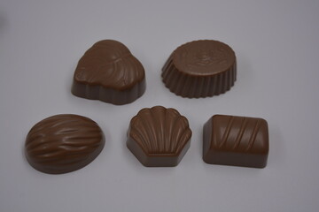 Food, food, very tasty milk candies are located on white plastic. Chocolates are made in the form of leaves, walnuts, medallions, round and square shapes.