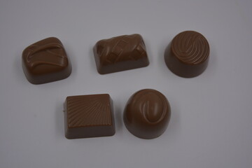 Food, food, very tasty milk candies are located on white plastic. Chocolates are made in the form of leaves, walnuts, medallions, round and square shapes.