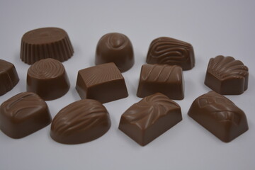 Food, food, very tasty milk candies are located on white plastic. Chocolates are made in the form of leaves, walnuts, medallions, round and square shapes.