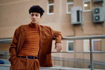 Stylish young man in brown suit and turtleneck poses against urban background