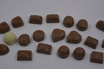Food, food, very tasty milk candies are located on white plastic. Chocolates are made in the form of leaves, walnuts, medallions, round and square shapes.