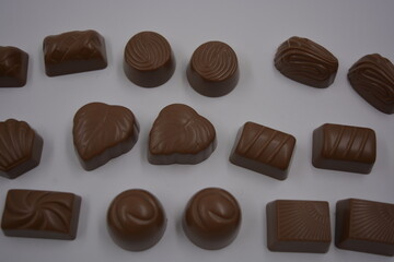 Food, food, very tasty milk candies are located on white plastic. Chocolates are made in the form of leaves, walnuts, medallions, round and square shapes.