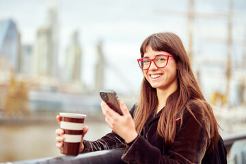 portrait young commuter business woman standing holding mobile phone and coffee cup in urban setting
