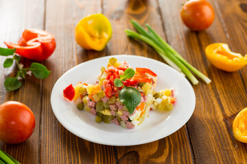 vegetable salad of boiled vegetables, with peas, sausage, sweet pepper. On a wooden table