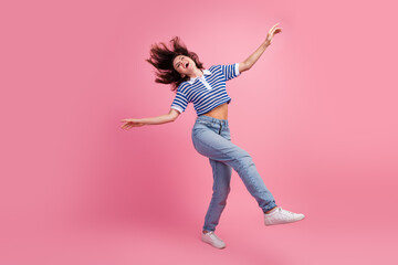 Joyful young woman dancing in casual style on pink background, radiating happiness and modern vibes
