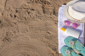 Beach essentials: towel, hat, sunglasses, sunscreen, and sandals on sandy beach