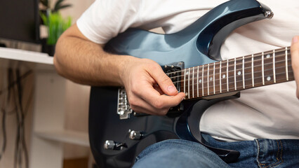 Fototapeta premium Close up young man playing string instrument, learning chords practicing music, enjoying rehearsal on electric guitar at home.