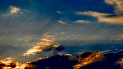 Blue sky, white, yellow and orange different types of clouds illuminated during sunset on windy weather - abstract background with natural pattern of clouds. Topics: air space, atmosphere, meteorology