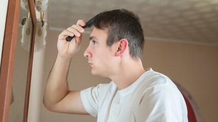 Young man comb his hair looking in the mirror at the bedroom.