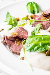 Tender slices of beef served with a creamy sauce, garnished with fresh greens and crispy toppings. A delicious and elegantly plated dish perfect for gourmet cuisine.