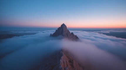 Fototapeta premium Rocky mountain peak piercing through a sea of clouds at sunrise with a soft orange and blue sky.