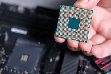 close-up of a cpu being held by hand with a motherboard in the background, showcasing gold pins and...
