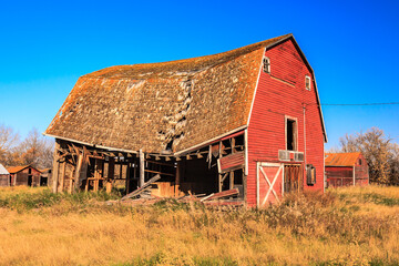 A red barn with a broken roof sits in a field