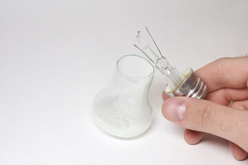 incandescent lamp base in mans hand. glass bulb divide and fell out by crack at rim of base. showing of broken light lamp