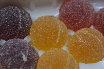 Original jelly Finnish candies in the form of round balls covered with white sugar. Yellow, orange, cherry, red gummy candies are arranged in white plastic packaging.