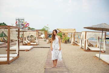 Woman Walking Barefoot on Wooden Pathway in Beach Resort with Elegant Cabanas