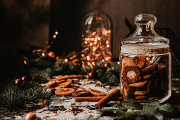 A rustic holiday setting featuring a jar of homemade cookies, surrounded by cinnamon sticks and festive lights. Pine branches add a cozy, warm atmosphere perfect for the winter season.