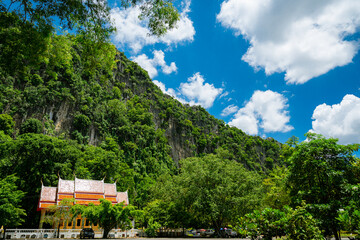 Fototapeta premium A rocky cliffs covered in lush green vegetation with orange roof of Wat Tum Khao Chakan, Sa Kaeo, Thailand