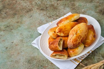 Pies with stewed fresh and pickled cabbage from yeast dough on a white ceramic dish on a green concrete background. Recipes cabbage.