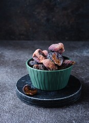 Dried dark figs in a green bowl on a green concrete background. Dried fruits. Ingredients for cooking.