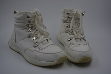 Things, household items, white shoes with an interesting sole, white laces. An unwashed, old, worn pair of women's shoes with metal rivets and a worn leather surface are located on a white plastic.