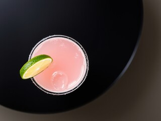 A refreshing pink cocktail garnished with a lime slice on a black surface.
