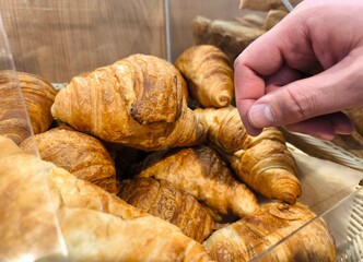A close-up of the buyer's hand of fresh pastries. The customer carefully takes fresh pastries and fresh croissants from the counter. fresh croissants in the store.