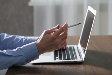 Businessman using laptop at wooden table indoors, closeup. Modern technology