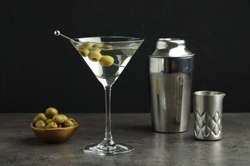 Martini cocktail with olives in glass and shaker on grey table against black background