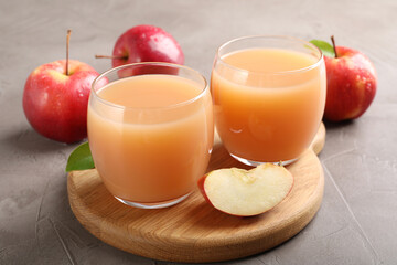 Tasty apple juice in glasses and fresh fruits on grey table, closeup