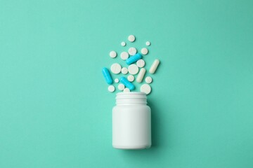 Various pills pouring out of medicine bottle on color background