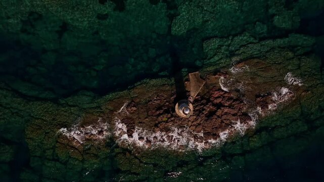 Rugged rocks and calm seas surround Faro Mangiabarche, Sardinia&rsquo;s iconic lighthouse. Captured by drone, the white foam, blue waters, and bright sunlight create a serene coastal masterpiece.