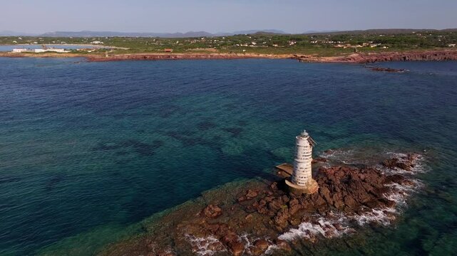 Faro Mangiabarche glows against Sardinia&rsquo;s calm blue seas. The drone films tranquil waves and rugged rocks, with bright sunlight completing this picturesque coastal view.