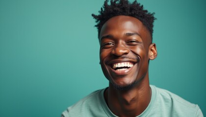 Obraz premium A cheerful young Black man with a radiant smile showcases pure joy, set against a striking teal backdrop. His infectious laughter and bright expression evoke feelings of warmth and positivity, making