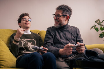 Father and son laughing while playing retro video games together at home - family bonding gaming and fun