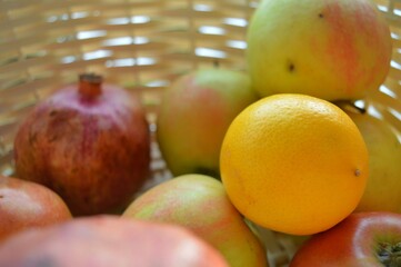 Close up photo sun rays on a wicker basket with apples pomegranates and oranges view from inside the basket. High quality photo