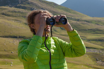 Hiker looking through binoculars on the mountain.
Traveler young man looking through binoculars outdoor.