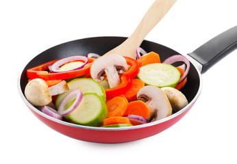 Frying pan with mix of fresh vegetables, mushrooms and spatula isolated on white