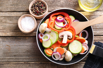 Frying pan with mix of fresh vegetables, mushrooms and spices on wooden table, flat lay