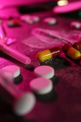Drug addiction. Different pills and syringe on table in color light, closeup